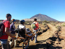 Una persona con movilidad reducida, junto a varios acompañantes, recorre en una joëlette un sendero del Parque Nacional del Teide (foto: FGN). Una persona con movilidad reducida, junto a varios acompañantes, recorre en una joëlette un sendero del Parque Nacional del Teide (foto: FGN).