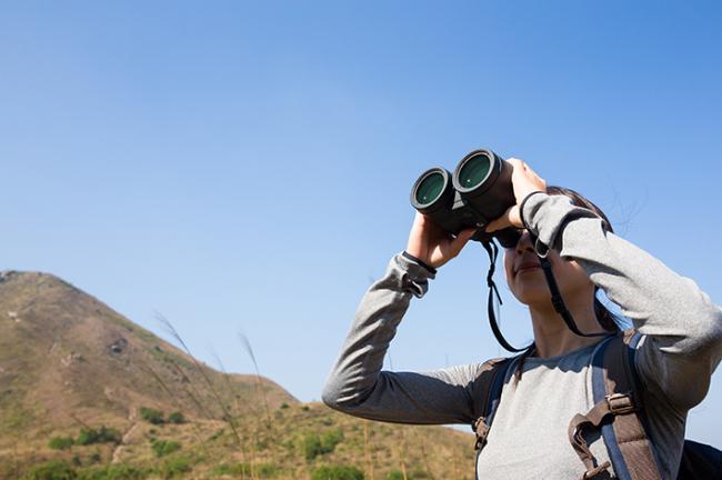 Una mujer observa a través de unos binoculares durante una salida naturalista (foto: Leung Cho Pan / 123RF).