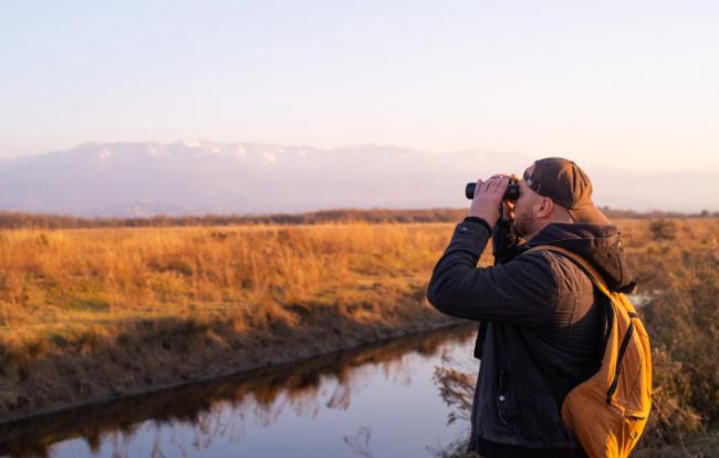 Un joven ornitólogo observa aves en un humedal (foto: isavira / Adobe Stock).